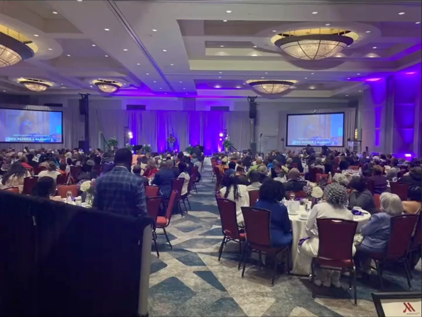 Conference ballroom with audience seating, projection screens, and purple lighting.